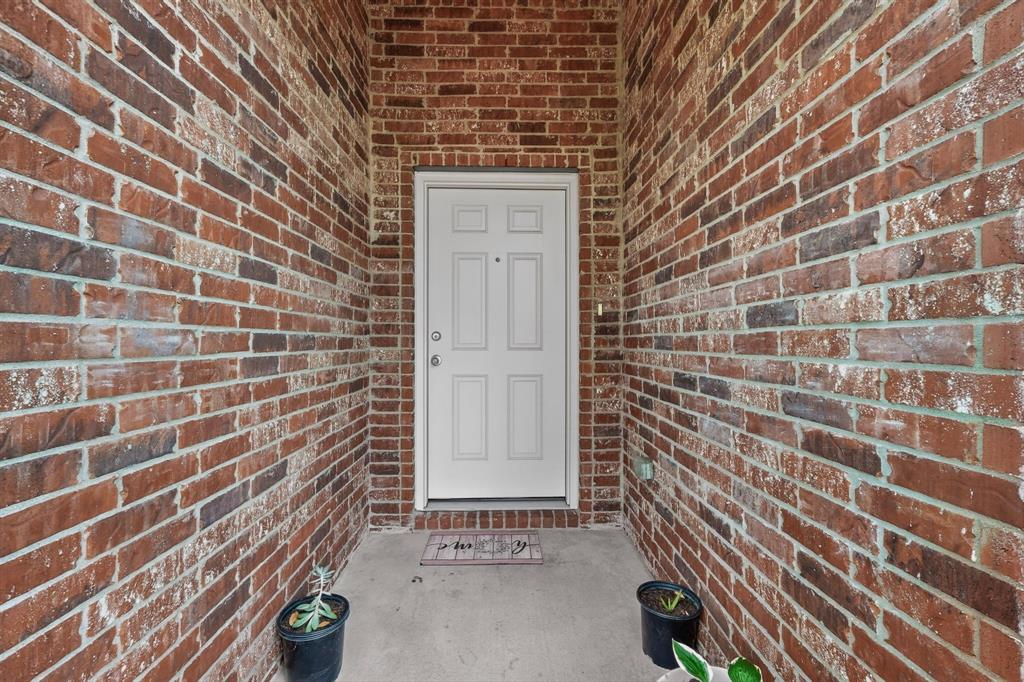 1409 Slate Street Princeton, TX 75407 - Photo 4 of 36 Recessed front entry with a panel-style door, brick exterior walls, concrete flooring, and an overhead light fixture