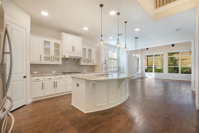 a large kitchen with kitchen island granite countertop a stove a sink a refrigerator a center island and a wooden floor