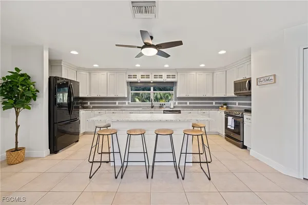 a kitchen with stainless steel appliances kitchen island granite countertop a refrigerator a stove a sink and white cabinets with wooden floor