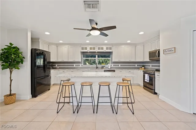 a kitchen with stainless steel appliances kitchen island granite countertop a refrigerator a stove a sink and white cabinets with wooden floor