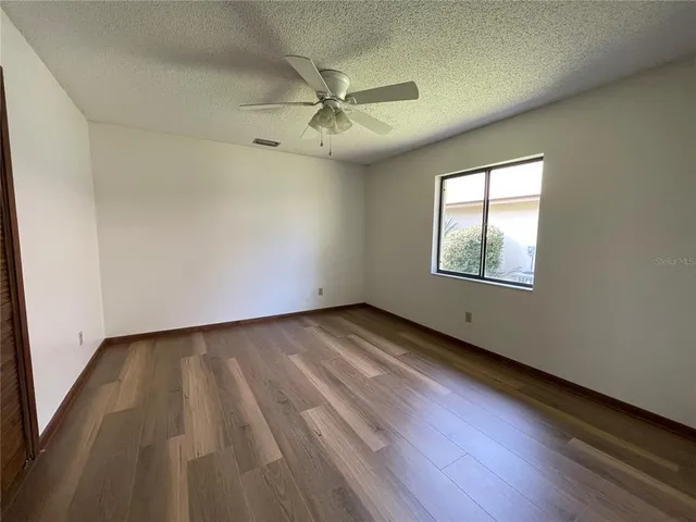 an empty room with wooden floor fan and windows