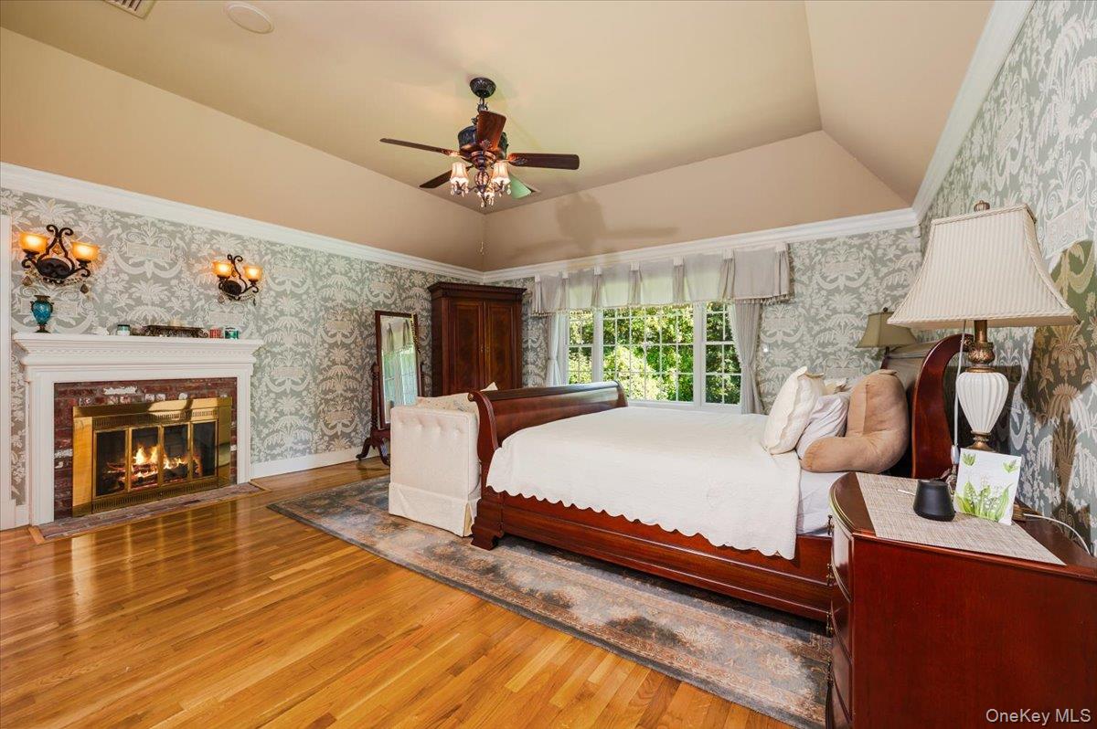 155 Jennings Road Cold Spring Harbor, NY 11724 - Photo 19 of 36 Bedroom featuring wallpapered walls, wood finished floors, a brick fireplace, lofted ceiling, and a ceiling fan