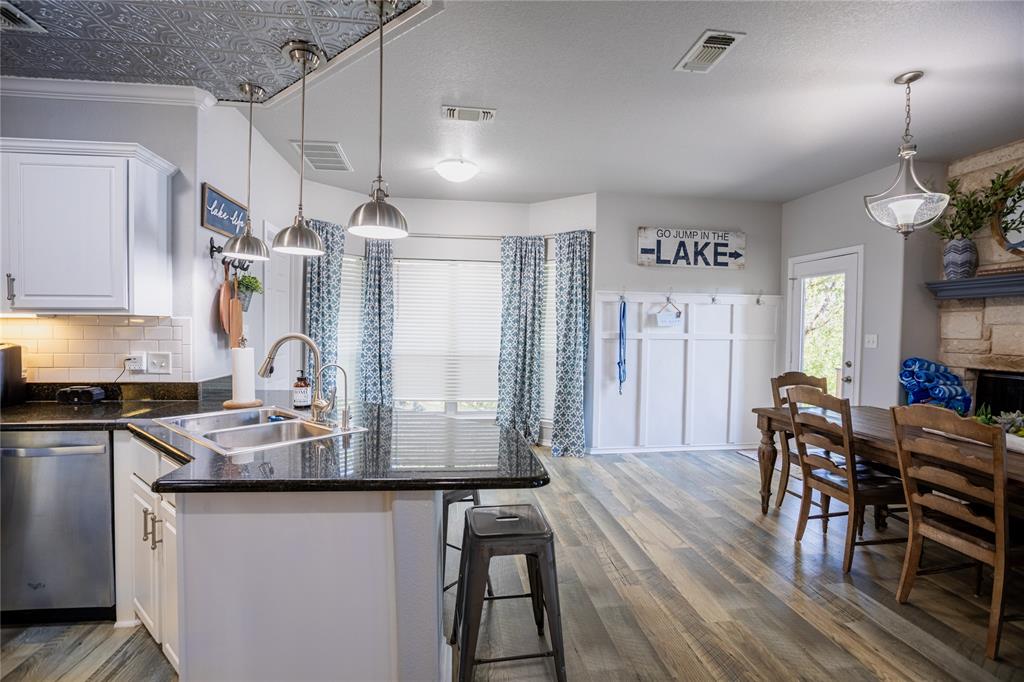 2702 River Ridge Court Granbury, TX 76048 - Photo 9 of 21 Kitchen featuring white cabinetry, a peninsula, dishwasher, a breakfast bar, and dark wood-type flooring