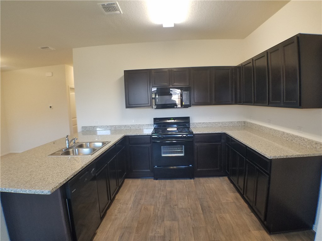 15016 Harkness Pass Austin, TX 78725 - Photo 9 of 25 a kitchen with a sink and a stove top oven with wooden floor