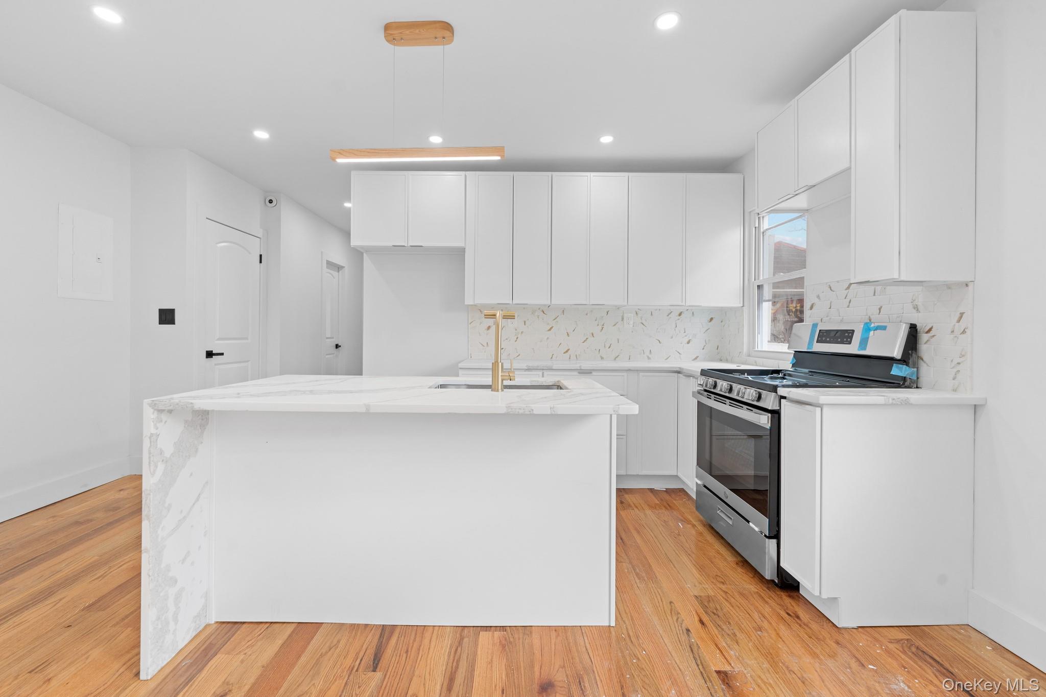 115-39 202nd Street Queens, NY 11412 - Photo 2 of 29 Kitchen featuring light stone counters, gas range, white cabinetry, an island with sink, and backsplash