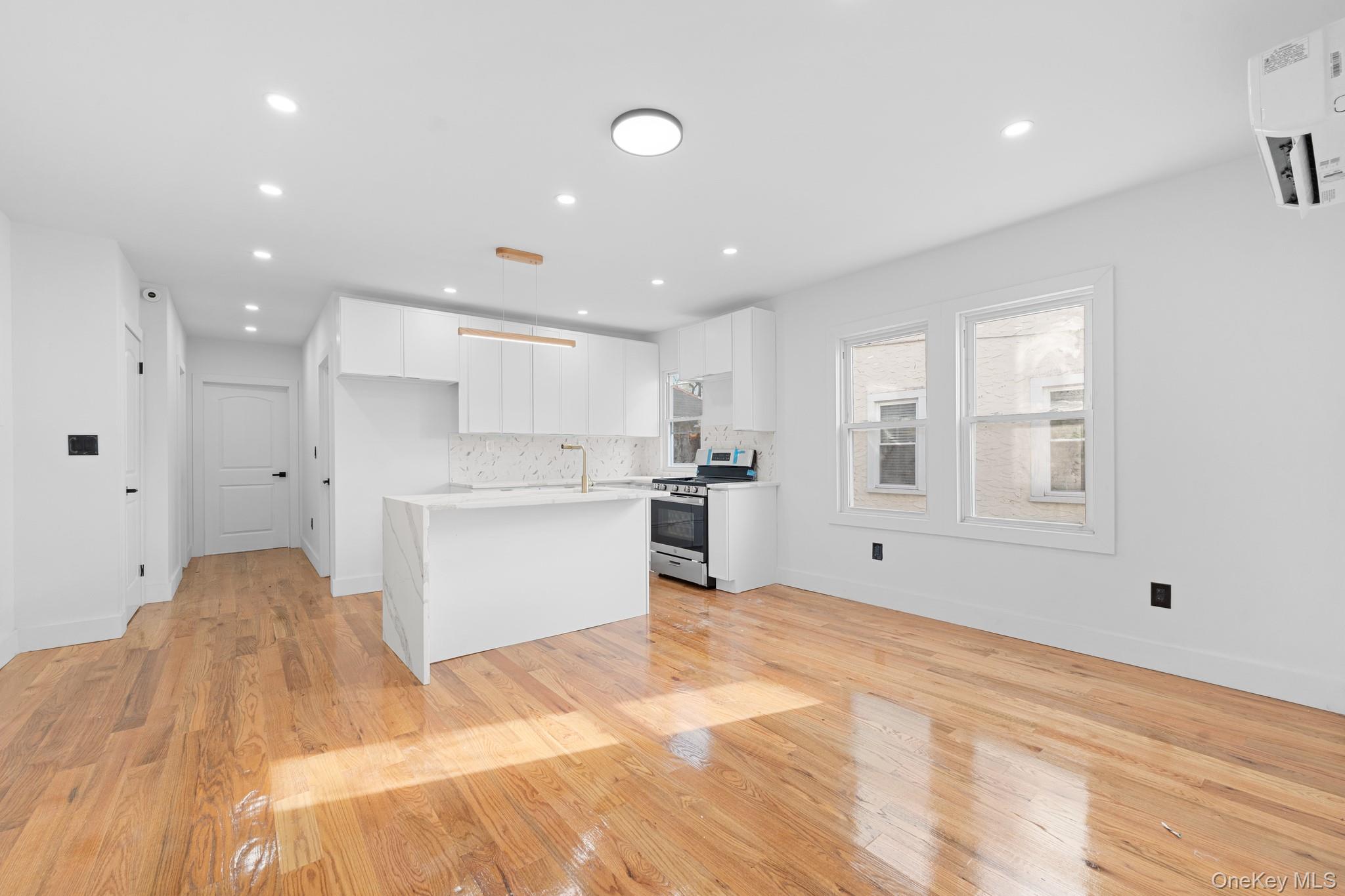 115-39 202nd Street Queens, NY 11412 - Photo 5 of 29 Kitchen featuring white cabinetry, an island with sink, decorative light fixtures, stainless steel gas range, and light wood-type flooring