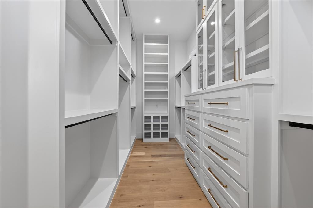11028 Edgemere Road Dallas, TX 75230 - Photo 28 of 40 Her Custom closet system featuring white cabinetry, glass-front upper cabinets, built-in drawers with brass hardware, open shelving, and wood-finish flooring