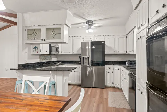 a kitchen with stainless steel appliances granite countertop a refrigerator a stove and white cabinets with wooden floor