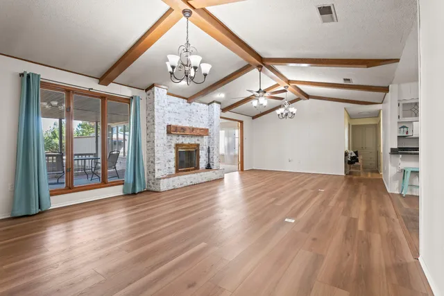 a view of an empty room with wooden floor and a kitchen