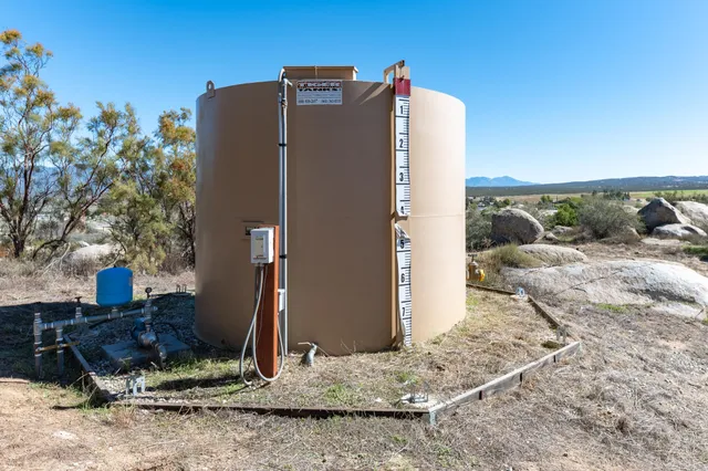 a view of a dry yard with trees in the background