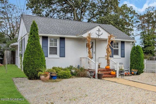 a view of a white house with potted plants and a large tree