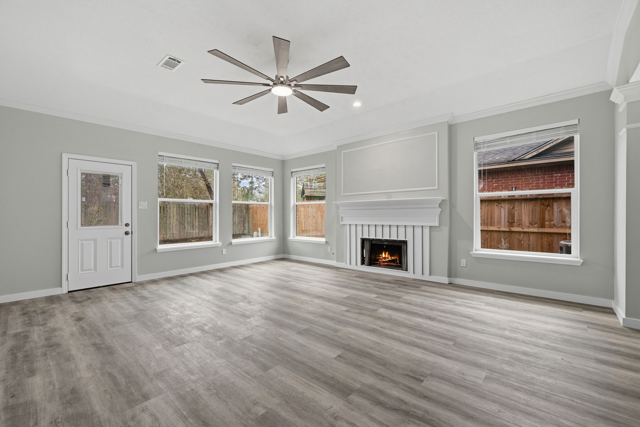 5411 Shady Maple Drive Houston, TX 77339 - Photo 13 of 28 This spacious living room features a modern ceiling fan, large windows for natural light, elegant fireplace, and sleek wood-look flooring, creating a cozy yet contemporary atmosphere.