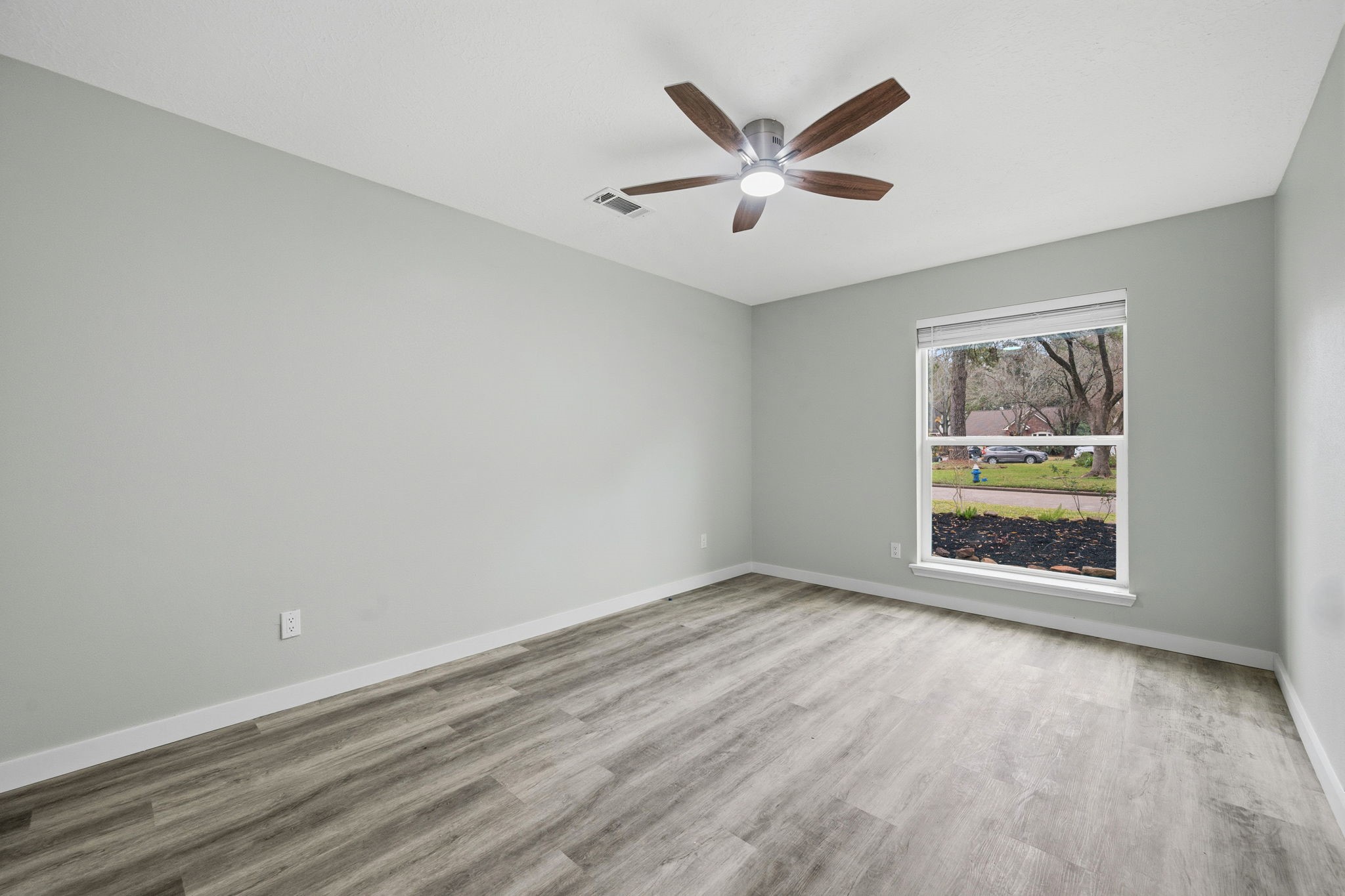 5411 Shady Maple Drive Houston, TX 77339 - Photo 16 of 28 This photo showcases a bright, spacious room with light gray walls, wood-look flooring, a ceiling fan, and a large window offering a view of the outdoors, perfect for a bedroom or office.