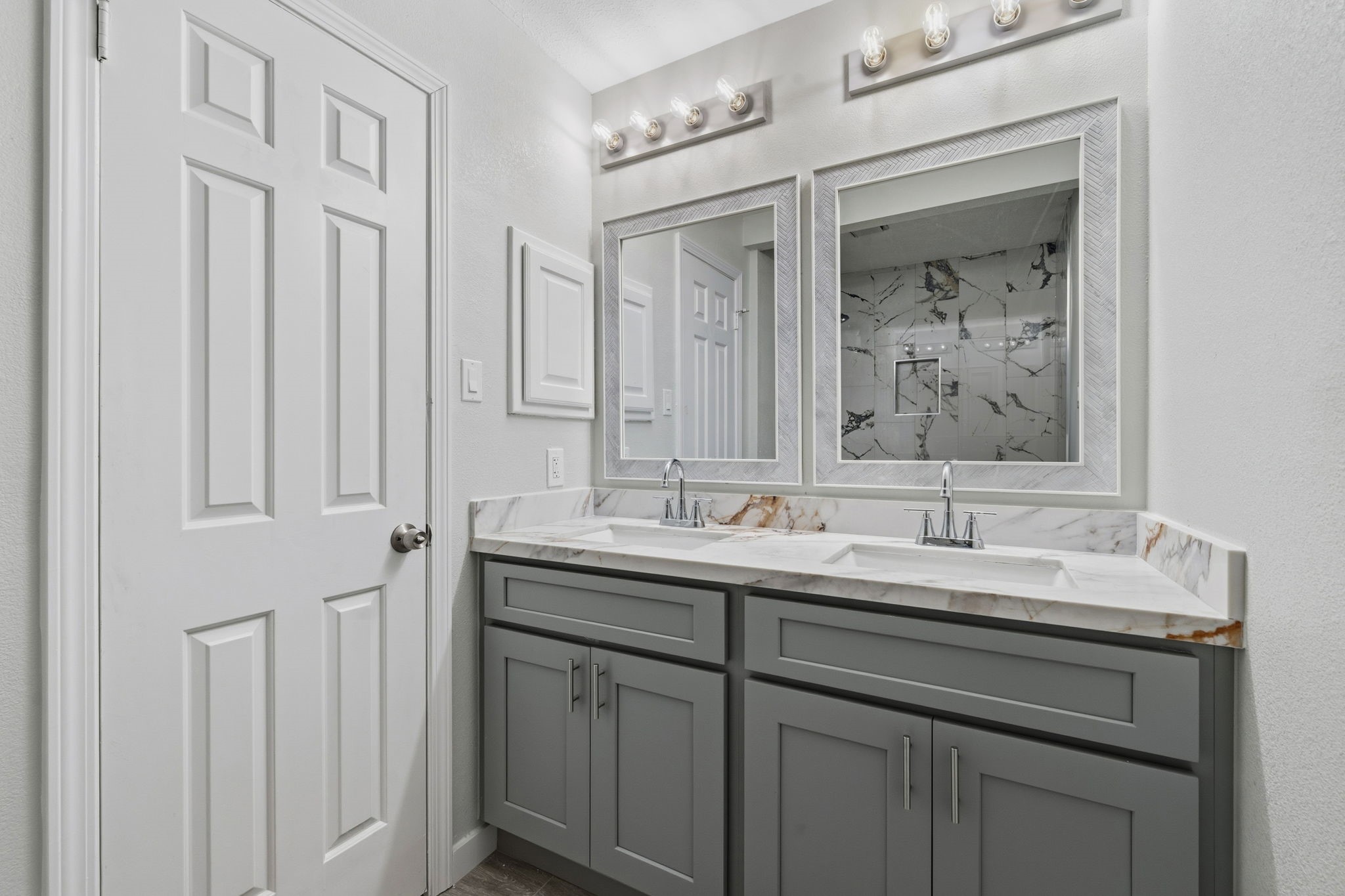 5411 Shady Maple Drive Houston, TX 77339 - Photo 18 of 28 This bathroom features a modern double vanity with sleek gray cabinets and marble countertops. Two large framed mirrors are illuminated by stylish light fixtures, and the space offers a clean, contemporary design with neutral tones.