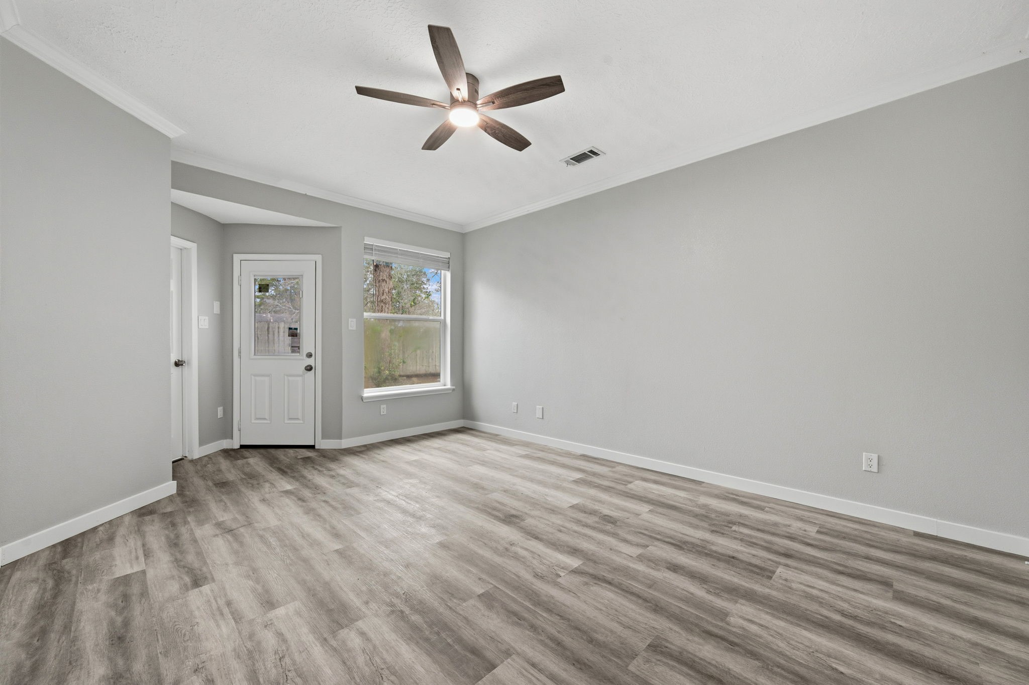 5411 Shady Maple Drive Houston, TX 77339 - Photo 20 of 28 This room features modern wood-look flooring, neutral gray walls, and a ceiling fan for comfort. Natural light fills the space through a large window, and there's a door leading outside, enhancing accessibility and brightness.