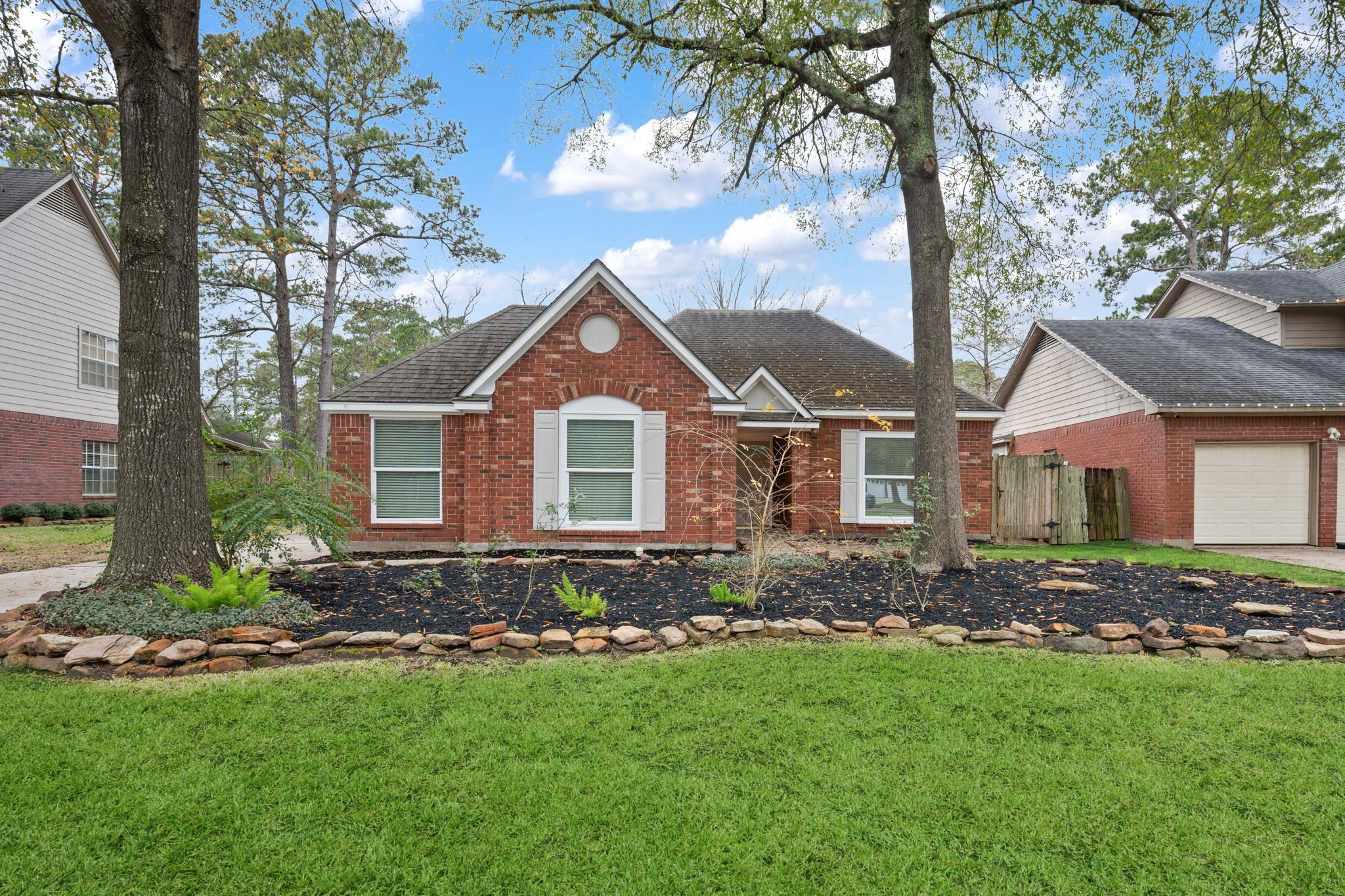 5411 Shady Maple Drive Houston, TX 77339 - Photo 2 of 28 Charming single-story brick home with a well-maintained front yard, featuring mature trees and a neat stone-bordered garden. The house has a gabled roof and large front windows, providing a welcoming and cozy appearance.