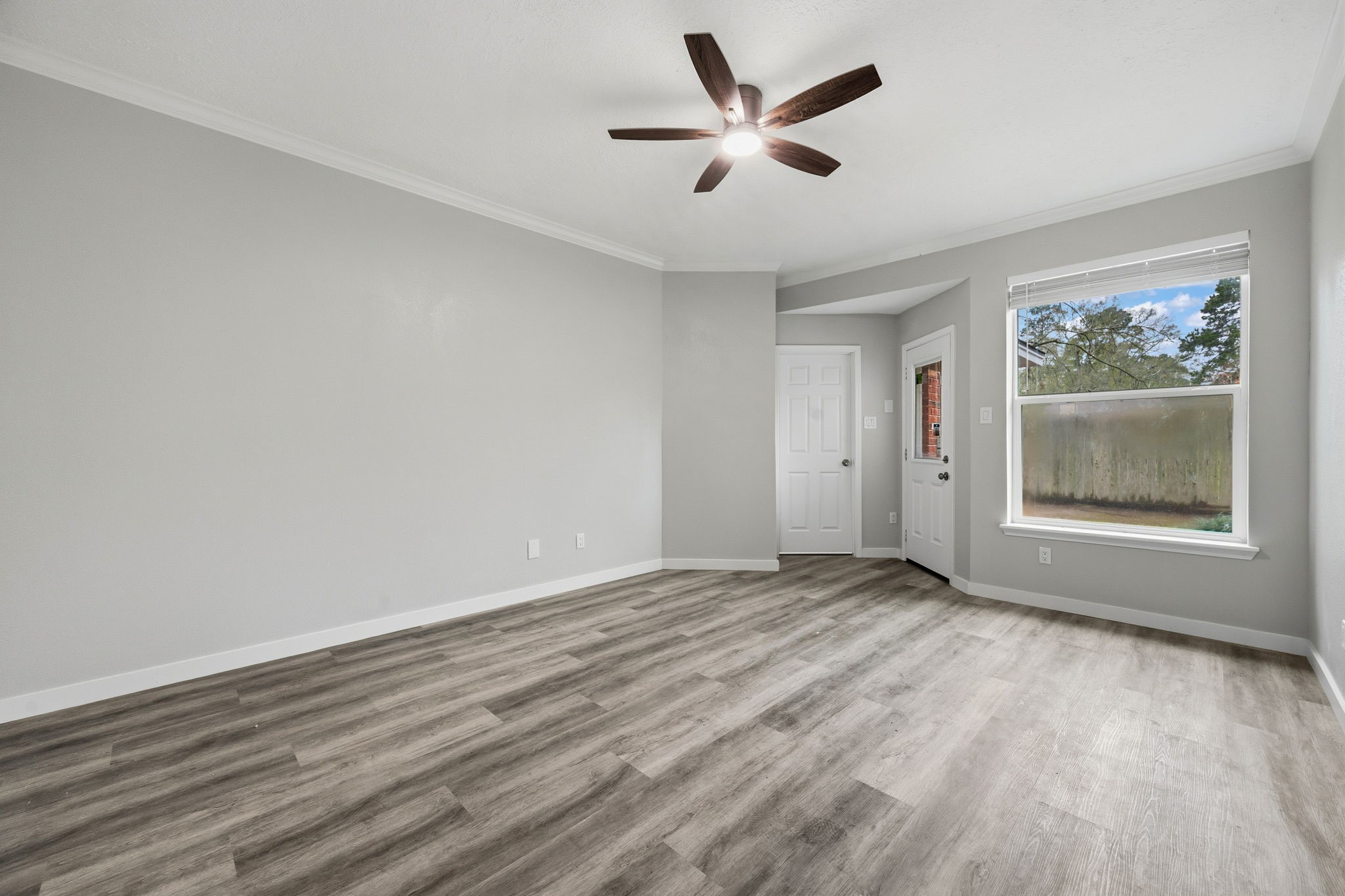 5411 Shady Maple Drive Houston, TX 77339 - Photo 21 of 28 This room features modern laminate flooring, soft gray walls, and a ceiling fan. It includes a large window for natural light and a door leading outside, creating a bright and inviting space.