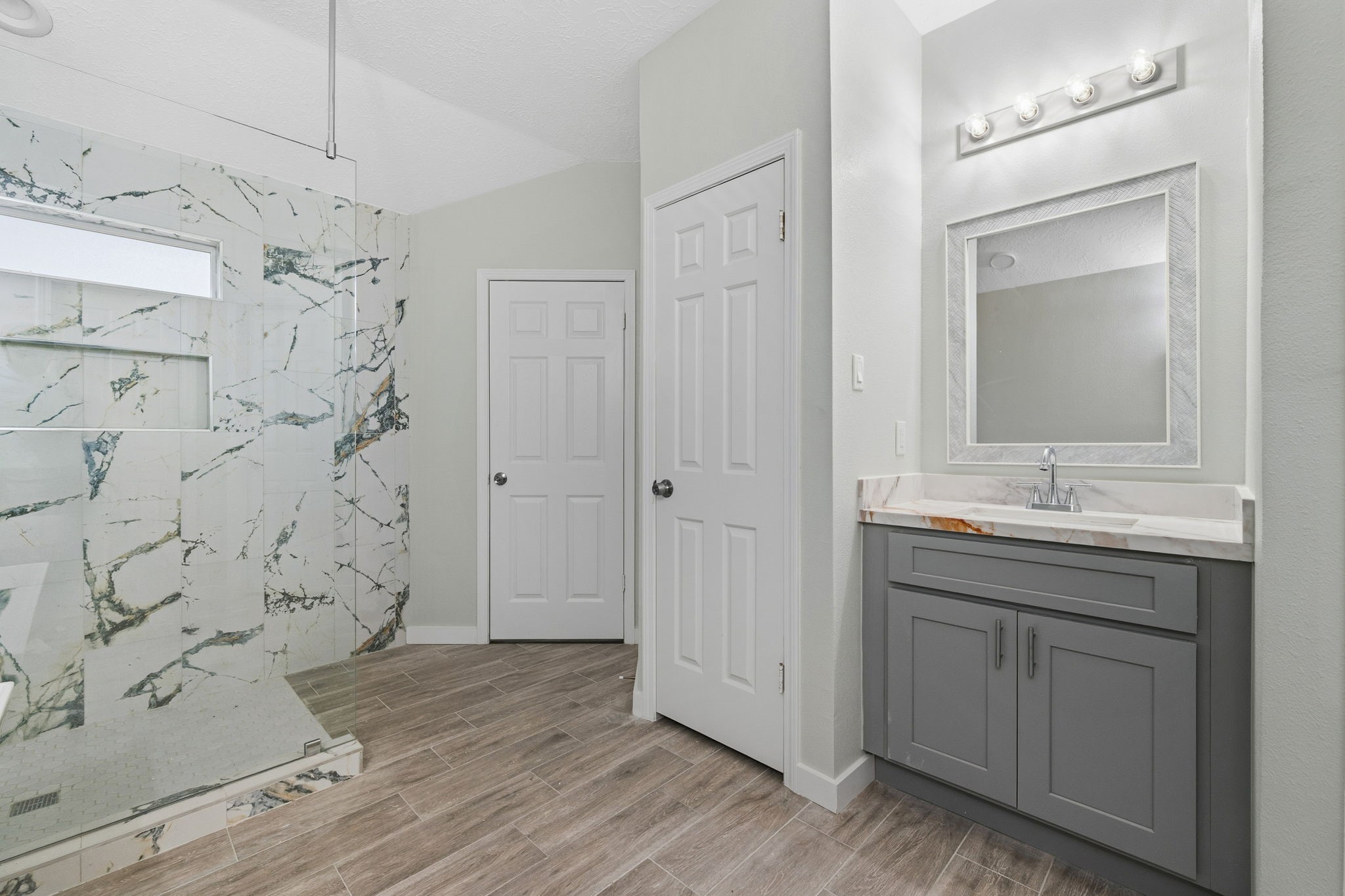 5411 Shady Maple Drive Houston, TX 77339 - Photo 22 of 28 This is a modern bathroom featuring a spacious shower with elegant marble-patterned tiles and a sleek vanity with a large mirror. The room is bright with neutral tones and wood-look flooring, creating a clean and inviting atmosphere.