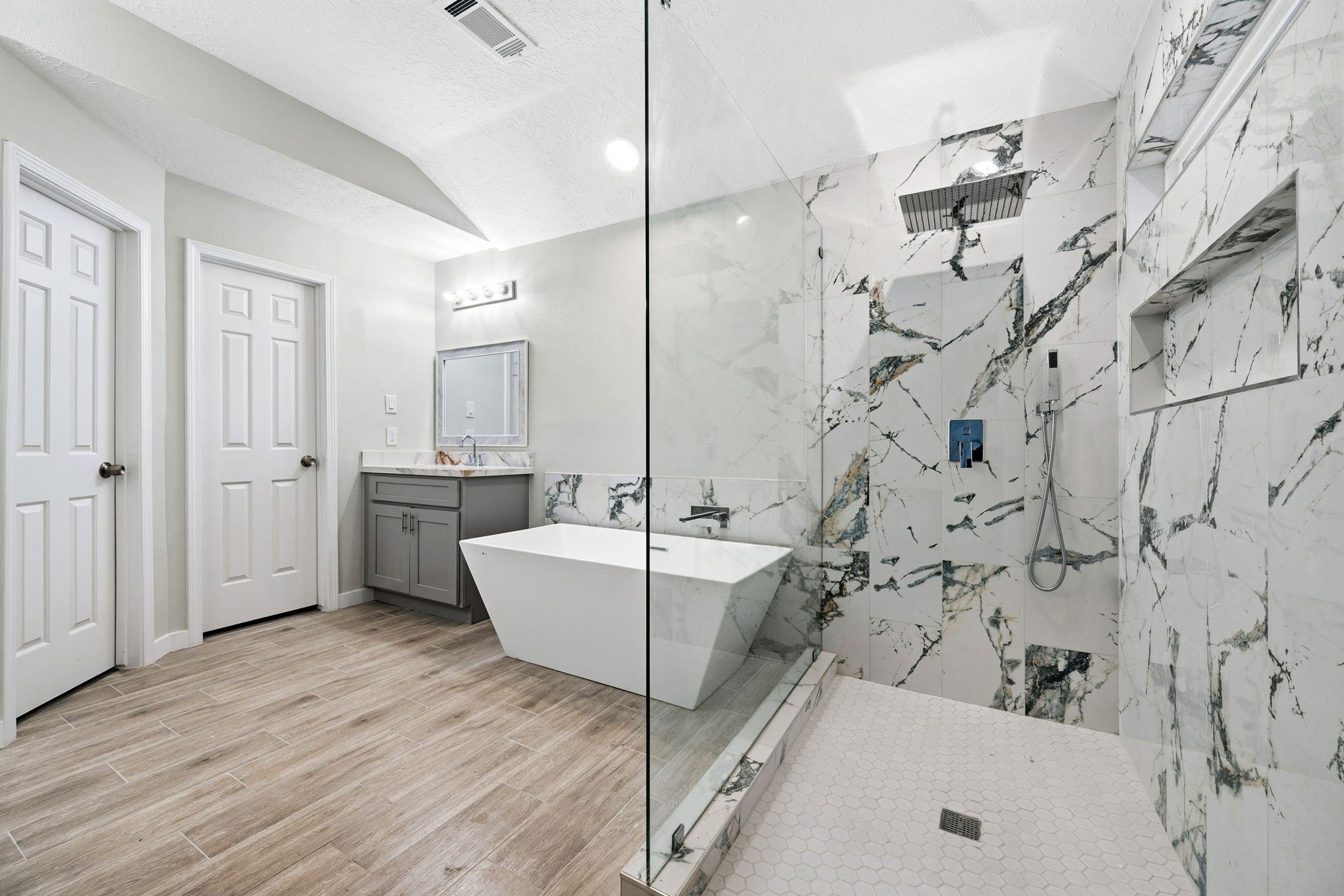 5411 Shady Maple Drive Houston, TX 77339 - Photo 27 of 28 This modern bathroom features a spacious walk-in shower with elegant marble walls, a sleek freestanding tub, and a stylish vanity with ample storage. The wood-look tile flooring adds warmth and sophistication.