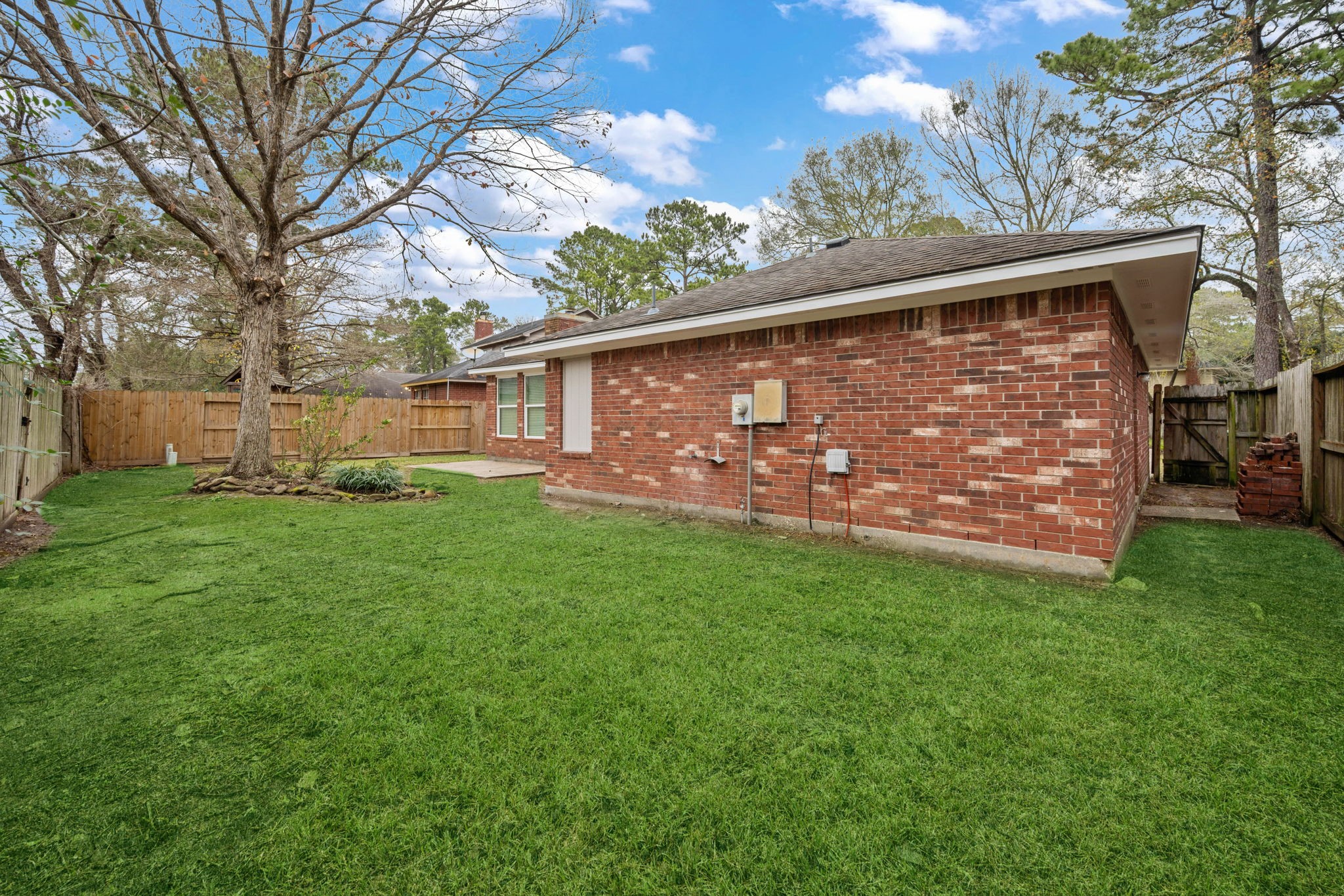 5411 Shady Maple Drive Houston, TX 77339 - Photo 4 of 28 This photo showcases a spacious backyard with a well-maintained lawn, a mature tree, and a brick exterior. The area is enclosed by a wooden fence, providing privacy and a welcoming outdoor space.