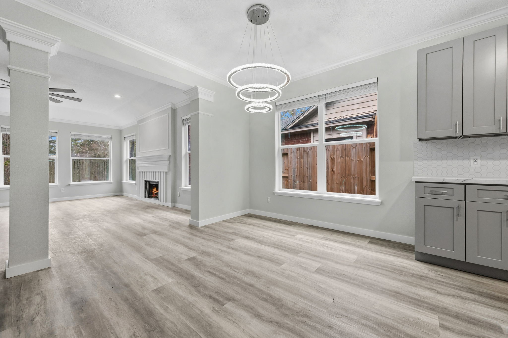 5411 Shady Maple Drive Houston, TX 77339 - Photo 7 of 28 This photo showcases a bright, open-concept living area with modern light fixtures and light wood flooring. It features large windows, a cozy fireplace, and grey cabinetry, offering a stylish and inviting space.