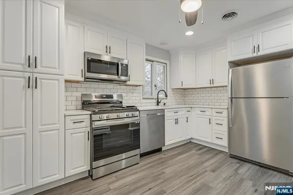 a kitchen with white cabinets stainless steel appliances and wooden floors
