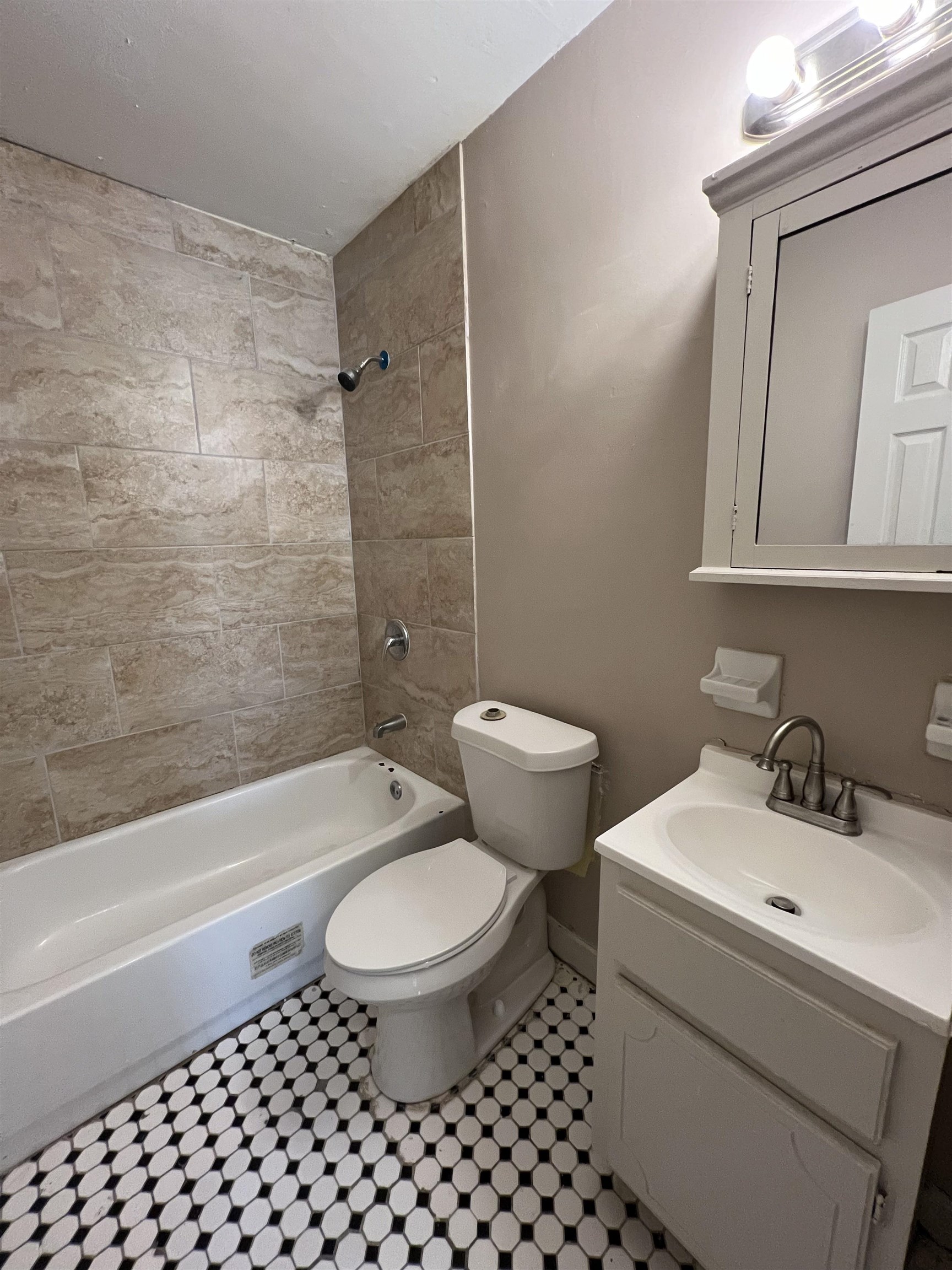 794 Nonconnah Road Memphis, TN 38109 - Photo 4 of 6 Black and white hexagonal floor tiles, full bathtub with a shower, textured wall tiles, white vanity with integrated sink, and a mirrored medicine cabinet