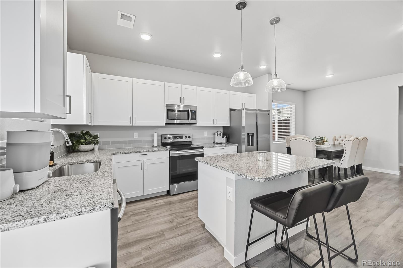 669 South Hoover Avenue Fort Lupton, CO 80621 - Photo 9 of 24 a kitchen with stainless steel appliances kitchen island granite countertop a sink a stove a dining table and chairs