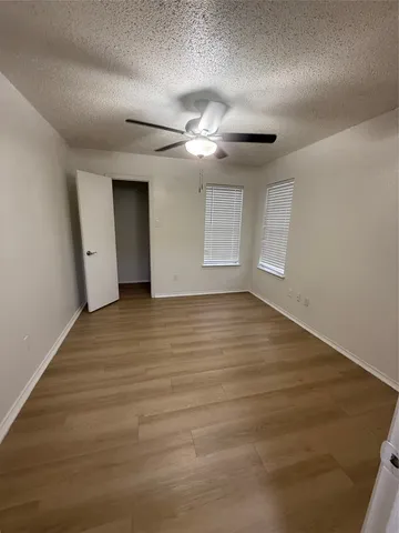 an empty room with wooden floor chandelier fan and windows