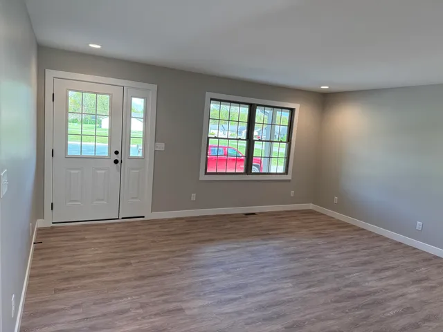a view of an empty room with wooden floor and a window