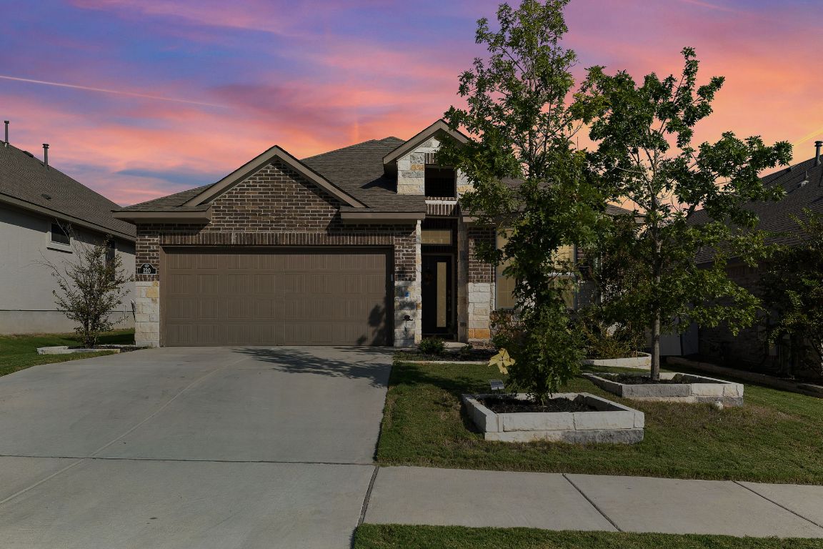 View of front of property featuring stone siding, brick siding, driveway, an attached garage, and a front lawn