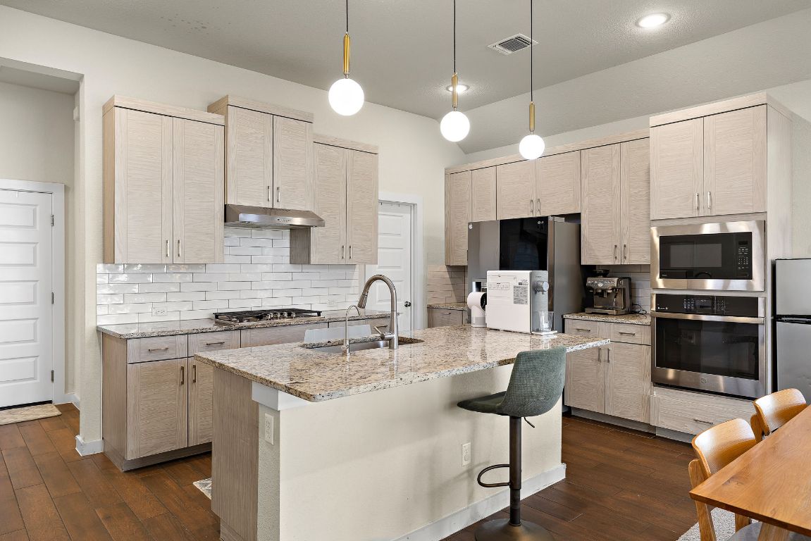 120 Upland Drive Georgetown, TX 78628 - Photo 8 of 21 Kitchen with hanging light fixtures, backsplash, light stone counters, and stainless steel appliances