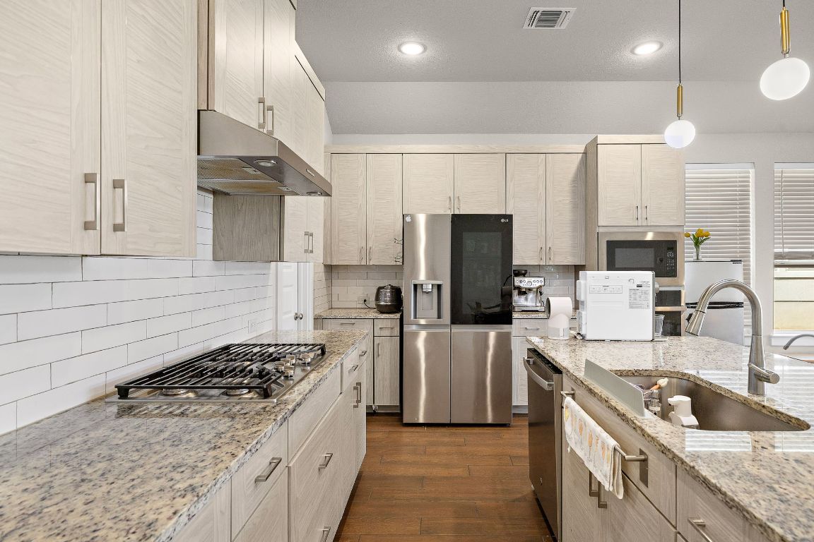120 Upland Drive Georgetown, TX 78628 - Photo 9 of 21 Kitchen featuring light stone countertops, backsplash, appliances with stainless steel finishes, dark wood finished floors, and hanging light fixtures