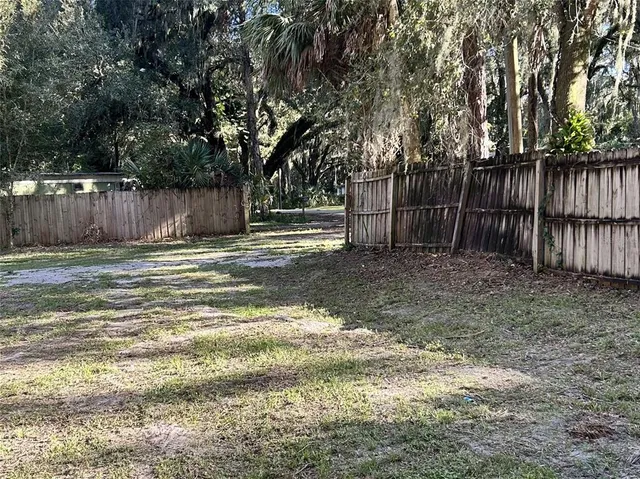 a view of a yard with large trees and wooden fence