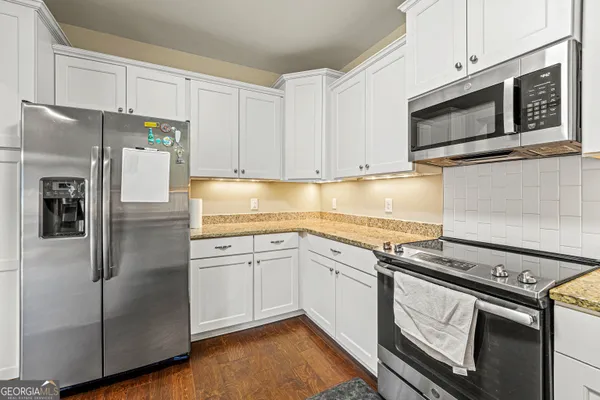 a kitchen with stainless steel appliances granite countertop a refrigerator a stove a sink and white cabinets
