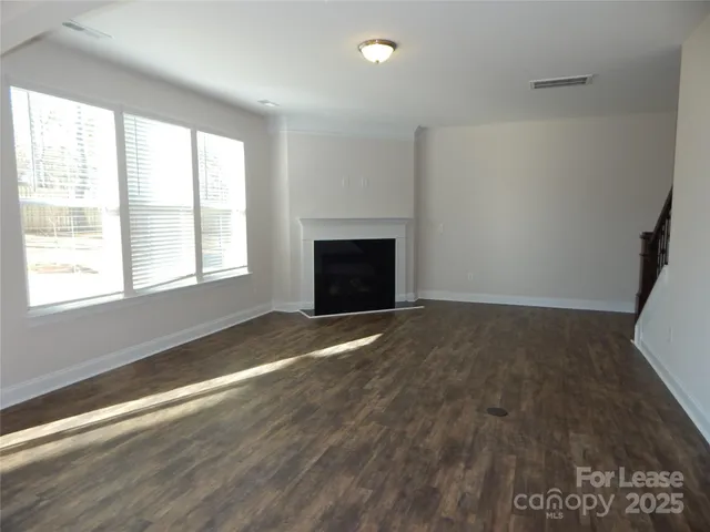an empty room with wooden floor fireplace and windows