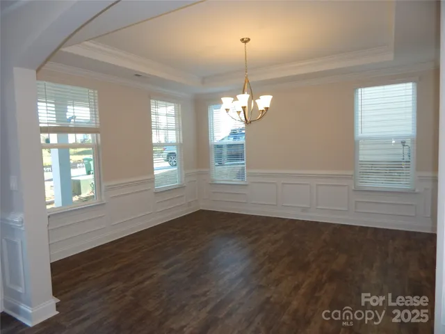 an empty room with wooden floor chandelier and windows