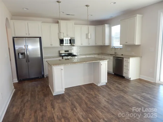 a kitchen with stainless steel appliances granite countertop white cabinets a refrigerator a sink a stove a microwave and wooden floors