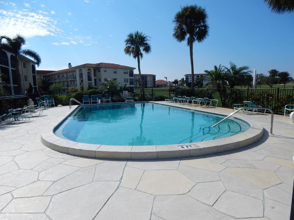 49 High Point Circle South, Unit 102 Naples, FL 34103 - Photo 31 of 31 a view of a swimming pool with a lounge chair and palm trees