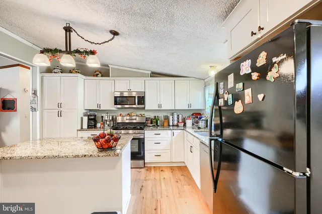 a kitchen with granite countertop a refrigerator a stove top oven and cabinetry