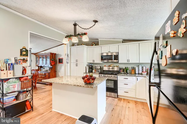 a kitchen with stainless steel appliances granite countertop a refrigerator a stove top oven a dining table and chairs with wooden floor