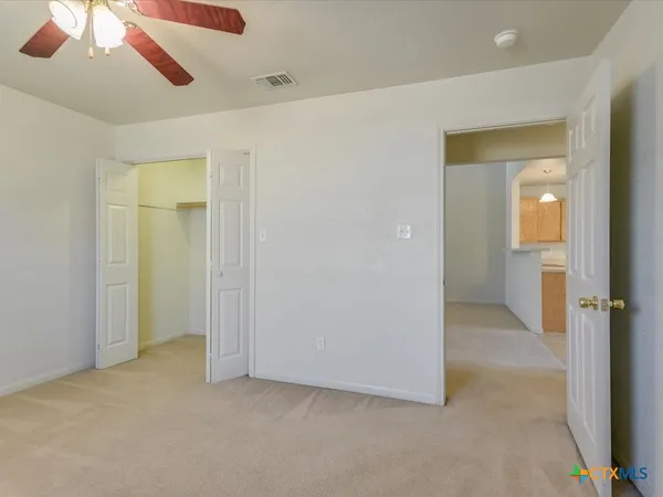 an empty room with chandelier fan and windows