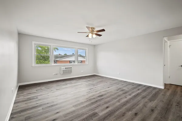 an empty room with wooden floor chandelier fan and windows