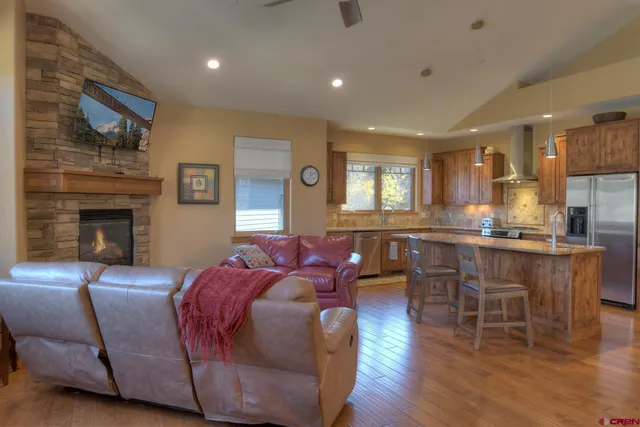 a living room with stainless steel appliances furniture wooden floor and a kitchen view