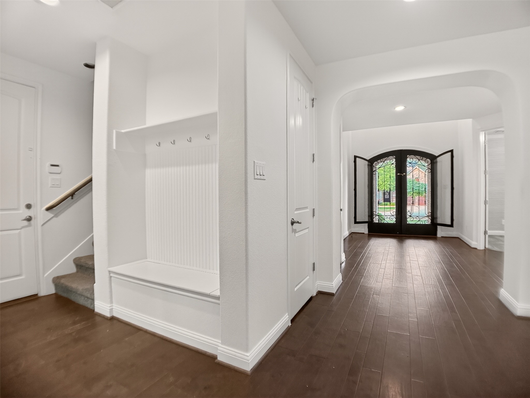 1505 Long Shadow Lane Georgetown, TX 78628 - Photo 4 of 28 Expansive foyer featuring dark wood-finish flooring, a built-in mudroom bench with hooks, a carpeted staircase with a wood handrail, and an arched entryway leading to decorative glass double doors