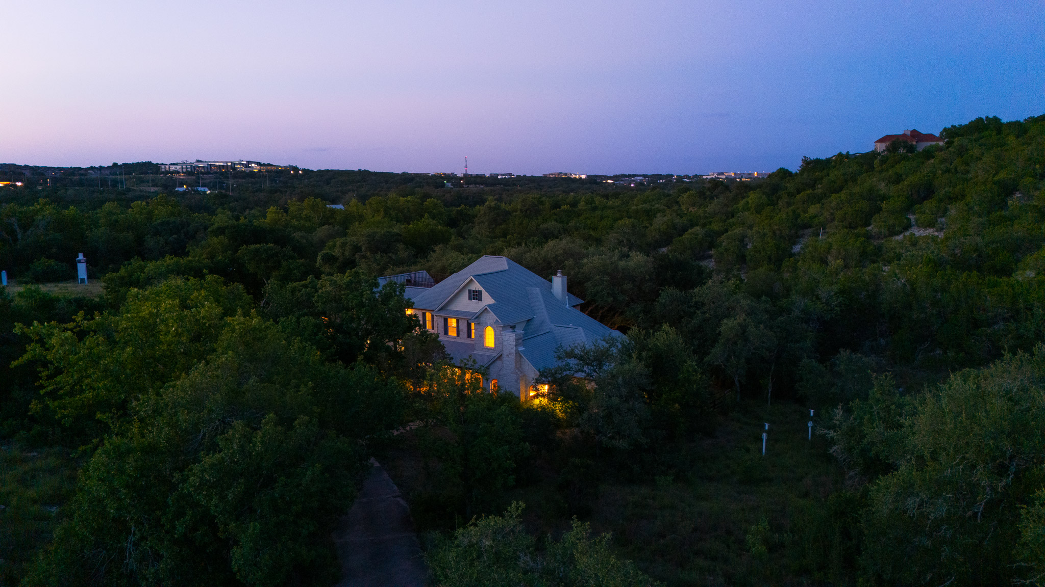 13800 Lone Rider Trail Austin, TX 78738 - Photo 32 of 32 Perched on a verdant hillside, this residence emanates a warm glow through its numerous windows as twilight descends.