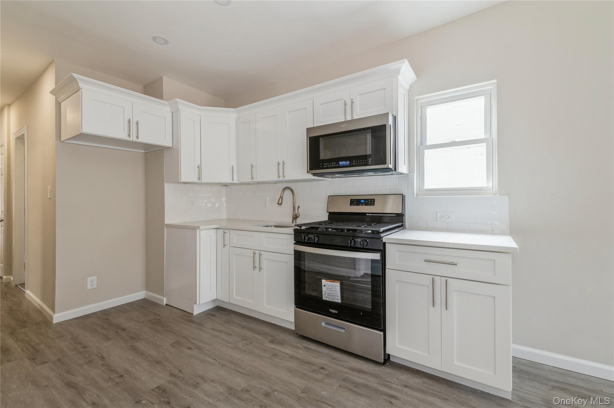 216-23 136th Road Queens, NY 11413 - Photo 12 of 28 Kitchen featuring stainless steel appliances, white cabinets, tasteful backsplash, and light wood-style flooring