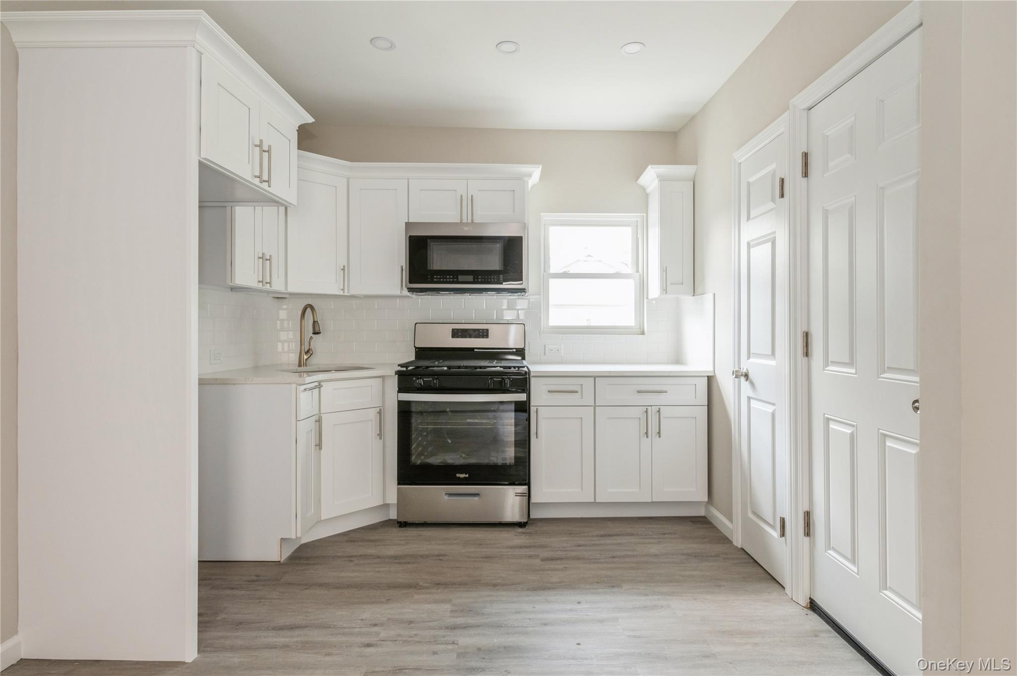 216-23 136th Road Queens, NY 11413 - Photo 15 of 28 Kitchen featuring stainless steel appliances, white cabinetry, light wood-style flooring, and backsplash