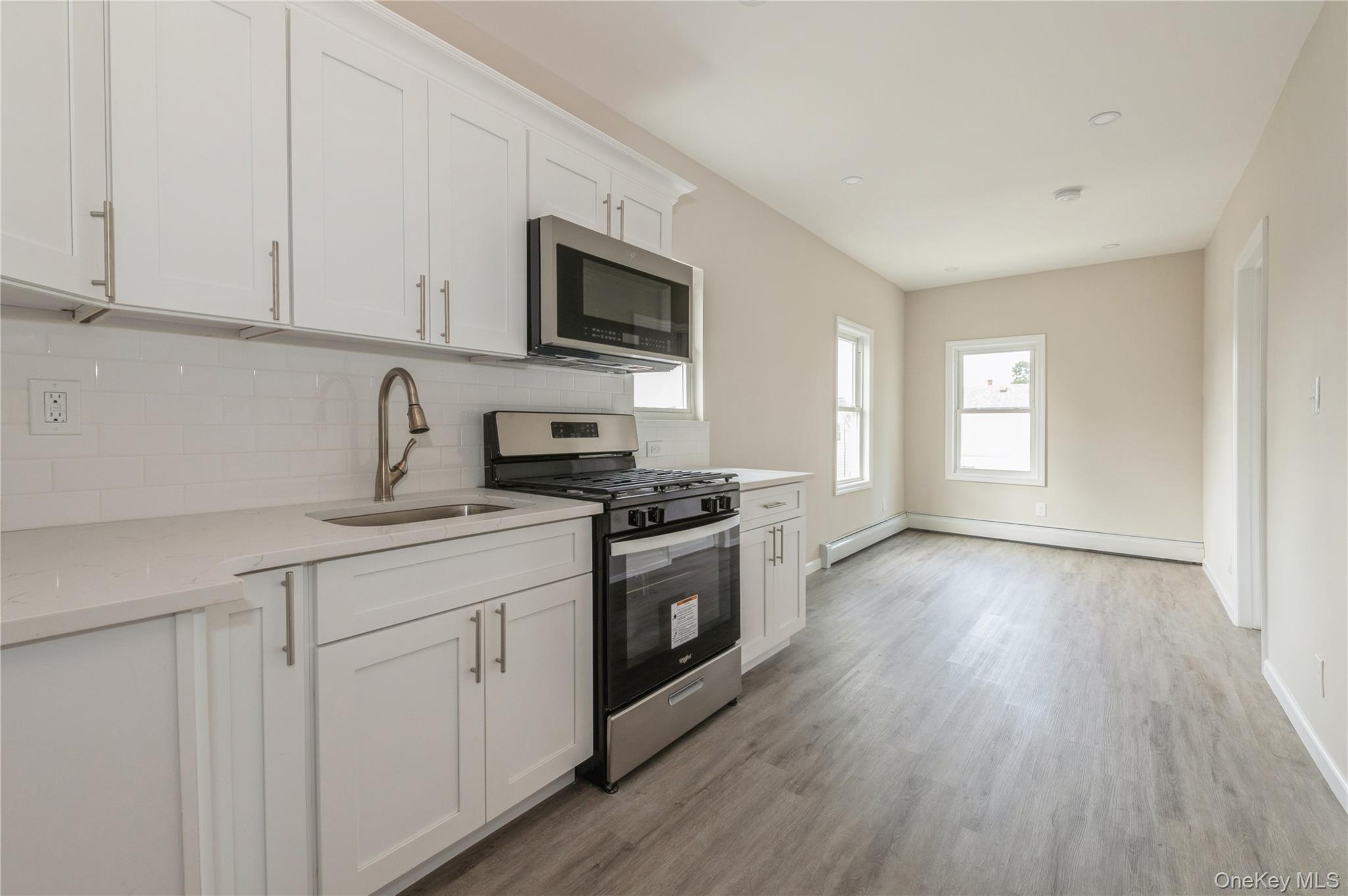216-23 136th Road Queens, NY 11413 - Photo 21 of 28 Kitchen with appliances with stainless steel finishes, white cabinetry, light stone countertops, tasteful backsplash, and light wood-type flooring