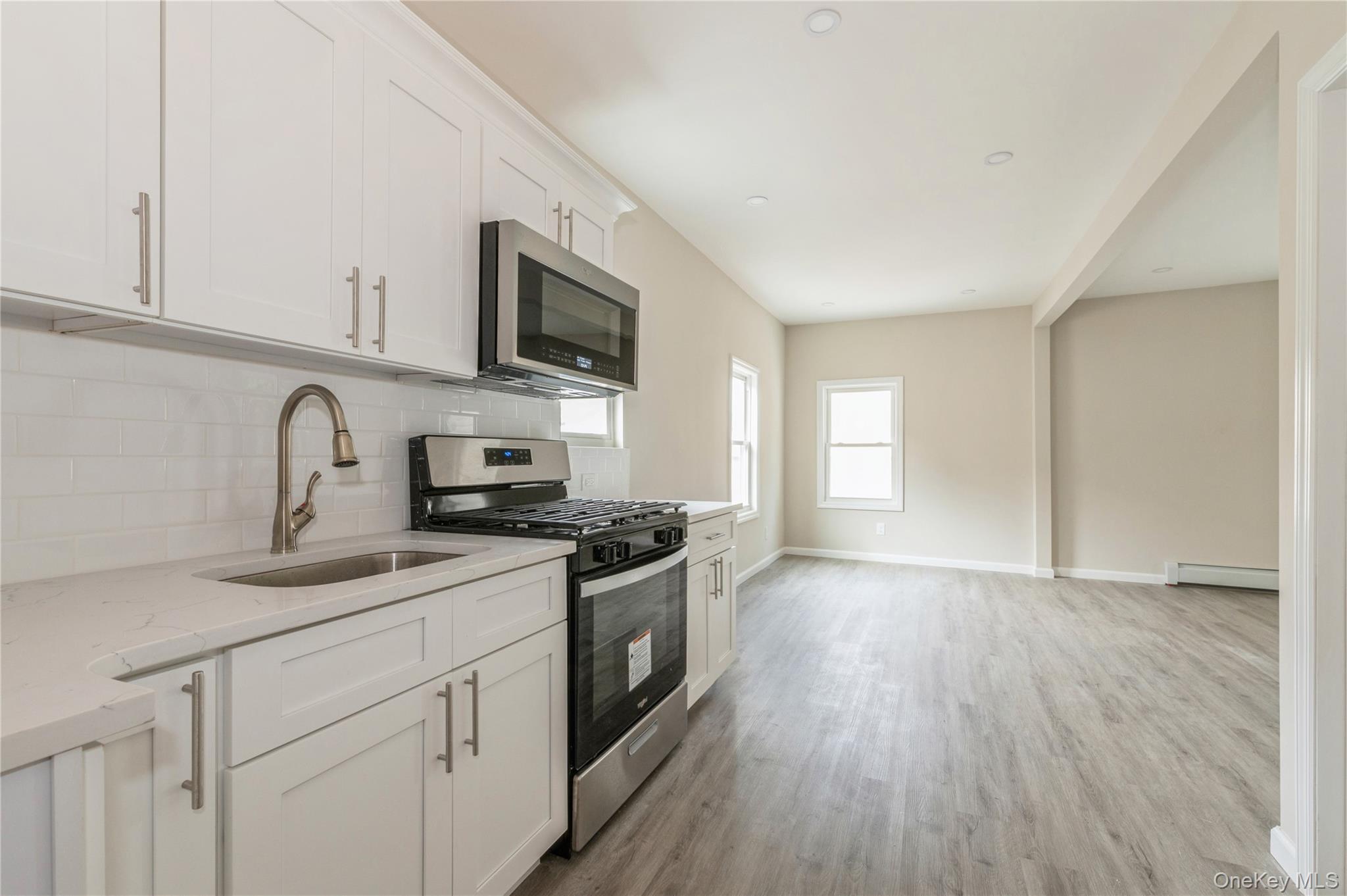216-23 136th Road Queens, NY 11413 - Photo 9 of 28 Kitchen featuring appliances with stainless steel finishes, white cabinetry, light stone countertops, light wood-type flooring, and backsplash
